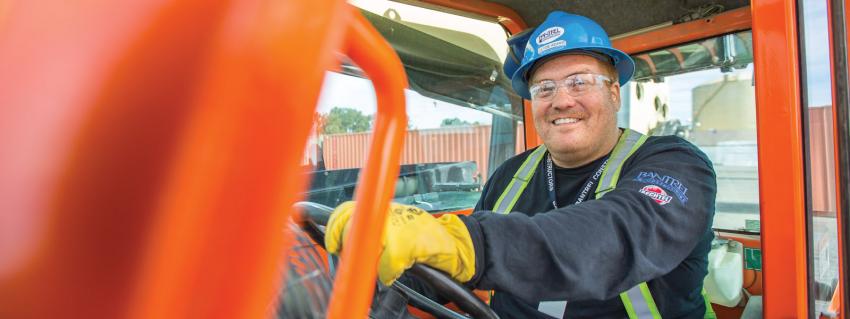 Man smiles at the camera sitting behind the wheel of a forklift