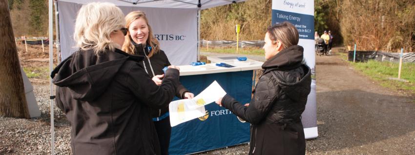 Three women talk in front of a FortisBC tent