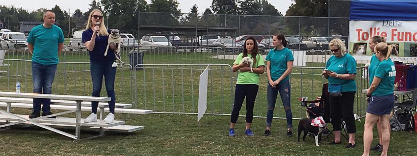 Woman speaks into microphone while holding a small dog while onlookers watch
