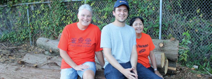 Three people sitting on a log smile at the camera