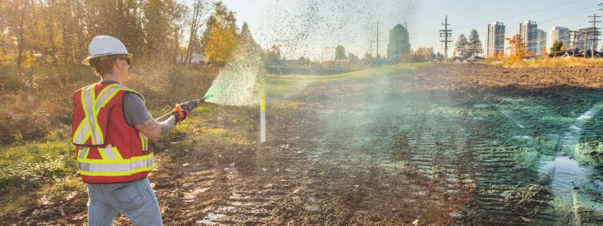 Man in hard hat and safety vest hoses down a muddy right of way