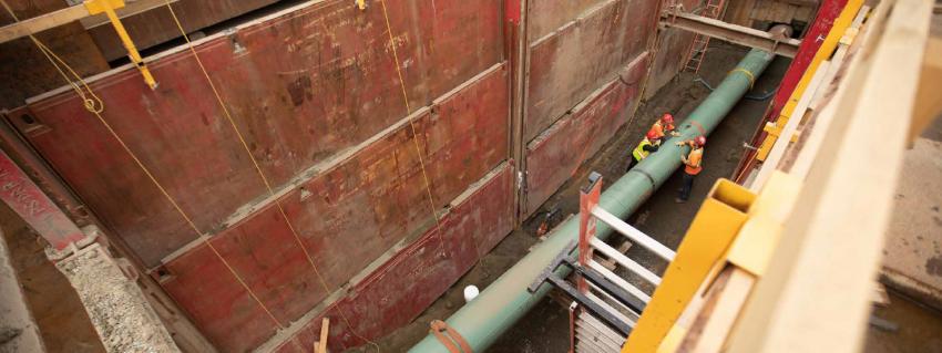 Looking down into a pipeline trench where three workers stand alongside a pipe