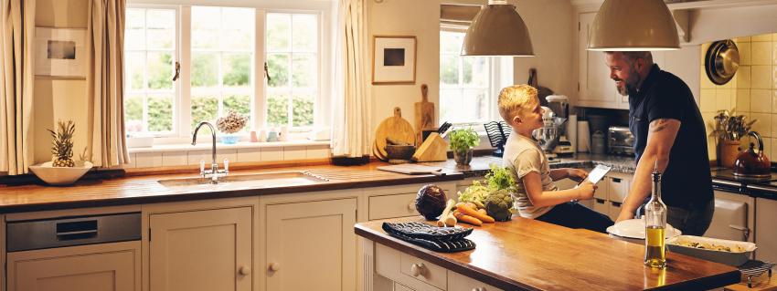 Man standing in kitchen laughing with boy sitting on counter