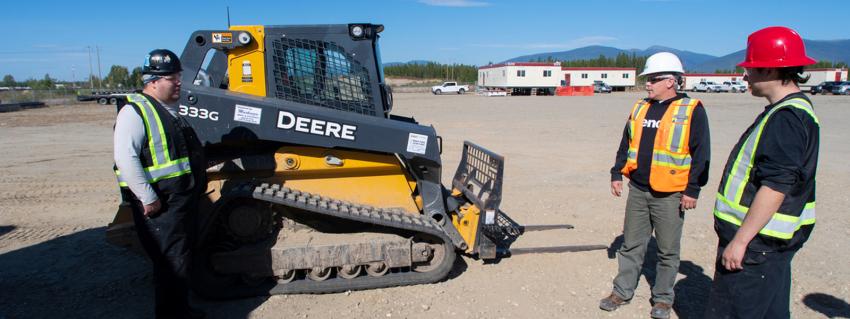 Three people stand in front of a bobcat machine