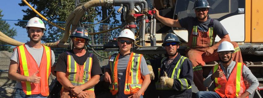 Six workers stand in front of a job site