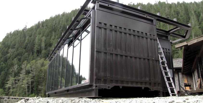 ContainerWest constructed a glass dining hall for a luxury wilderness retreat featuring floor to ceiling glass windows, a rustic wood interior and an upper deck with railings.