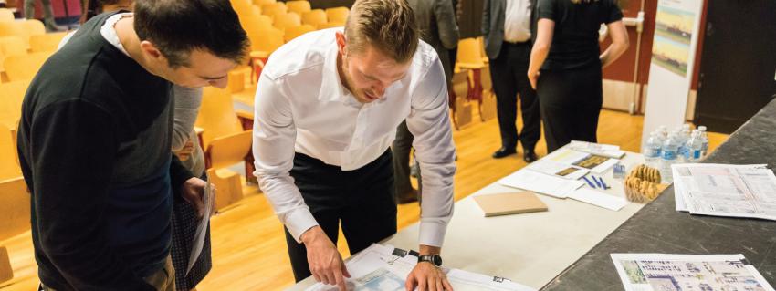 Two men look at blueprint drawings during a public meeting