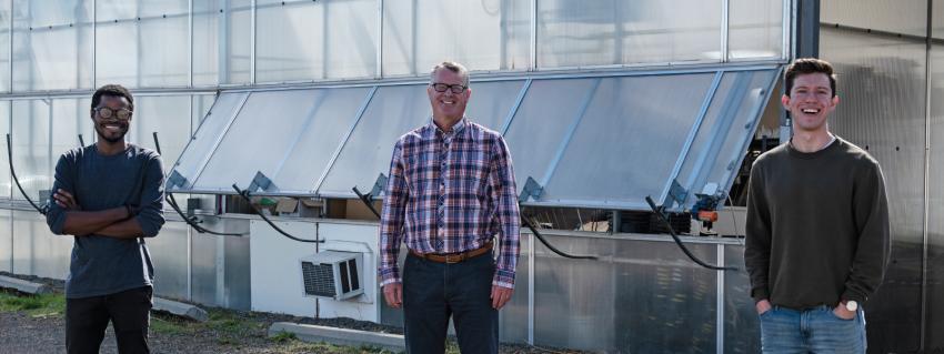 Three men stand in front of a greenhouse