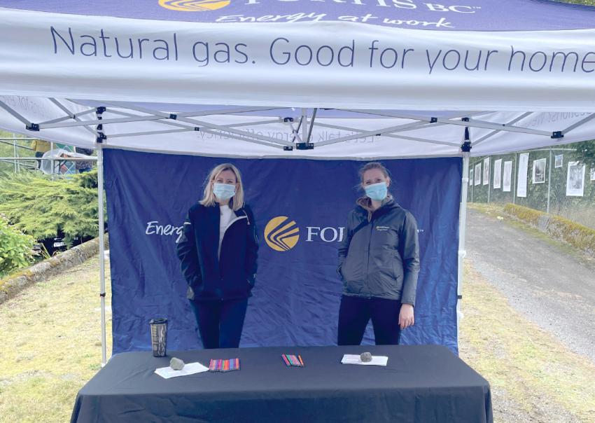 Two women wearing masks stand under a FortisBC tent