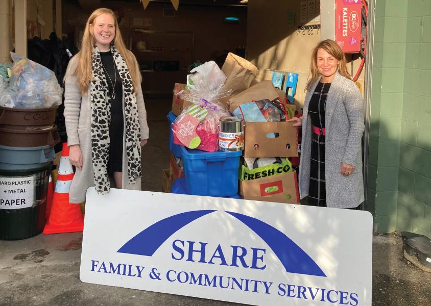 Two women stand behind a SHARE Family & Community Services banner