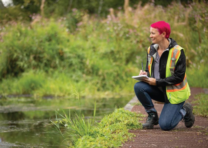 Caroline Astley kneels beside a waterway