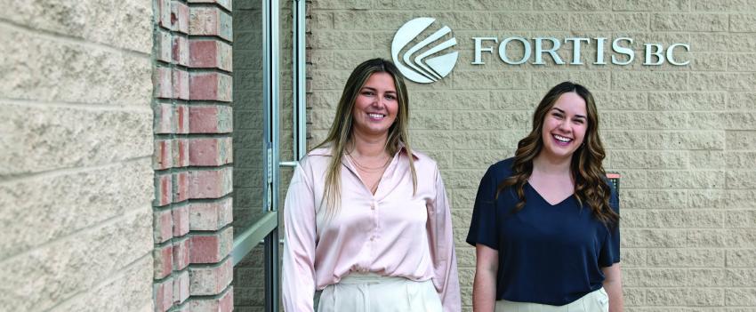 Two women smile outside a building with the FortisBC logo in the background