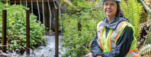 FortisBC employee wearing safety gear kneels beside a water culvert